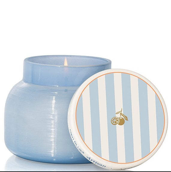 Blue candle in a textured jar with a striped lid on a white background