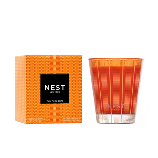 A NEST New York Pumpkin Chai scented candle shown with its orange patterned box and the clear glass candle vessel, both featuring orange-to-red gradient coloring, on a solid white background.